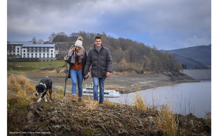 Ein Paar geht mit Hund am Hennesee spazieren.