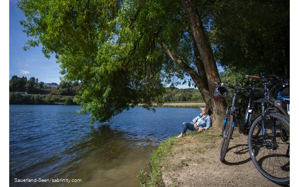 Radfahrerin genießt die Sonne am Seeufer