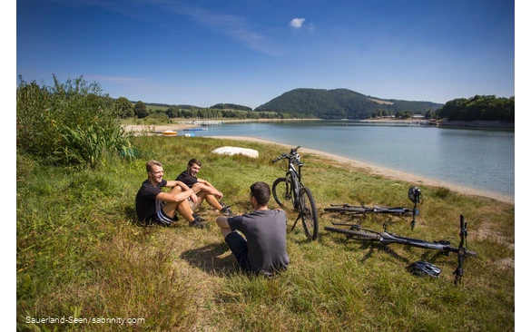 Eine Gruppe Jugendlicher macht Pause auf einer Wiese am See