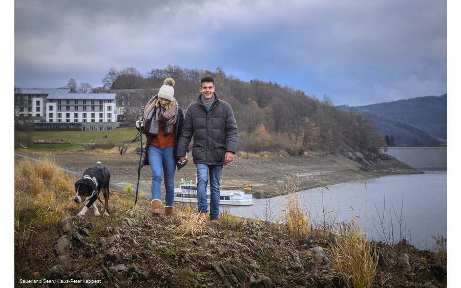 Ein Paar geht mit Hund am Hennesee spazieren.