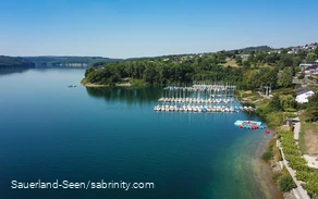 Drohnenaufnahme vom glasklaren blauen Wasser mit Segelbooten im Hintergrund