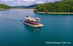 Drohnenaufnahme des elektrischen Personenschiffs auf dem Hennesee. Die Staumauer und Teile Meschedes sind im Hintergrund.