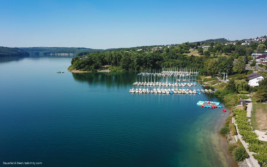 Drohnenaufnahme vom glasklaren blauen Wasser mit Segelbooten im Hintergrund