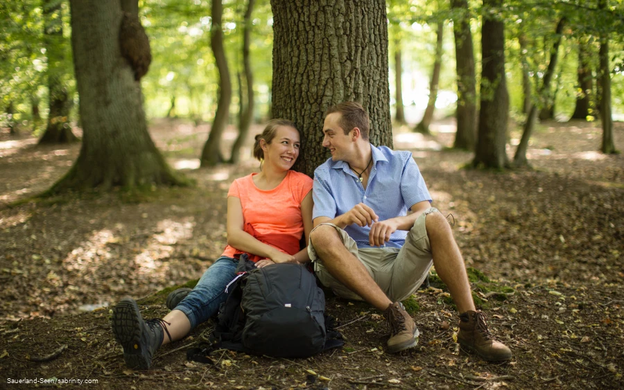 Ein Pärchen lehnt an einem Baumstamm und macht Pause