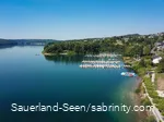 Drohnenaufnahme vom glasklaren blauen Wasser mit Segelbooten im Hintergrund