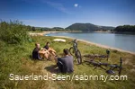 Eine Gruppe Jugendlicher macht Pause auf einer Wiese am See