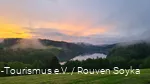 Über dem Hennesee und den Bäumen steigt Nebel auf und der Himmel kreiert mit Wolken und der unterhehenden Sonne ein Farbspektakel.