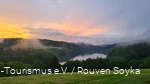 Über dem Hennesee und den Bäumen steigt Nebel auf und der Himmel kreiert mit Wolken und der unterhehenden Sonne ein Farbspektakel.